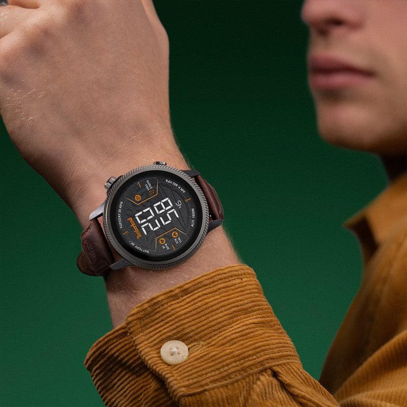 Timberland Trail Force smartwatch with a rugged dark case and brown leather strap worn on a wrist against a green background.